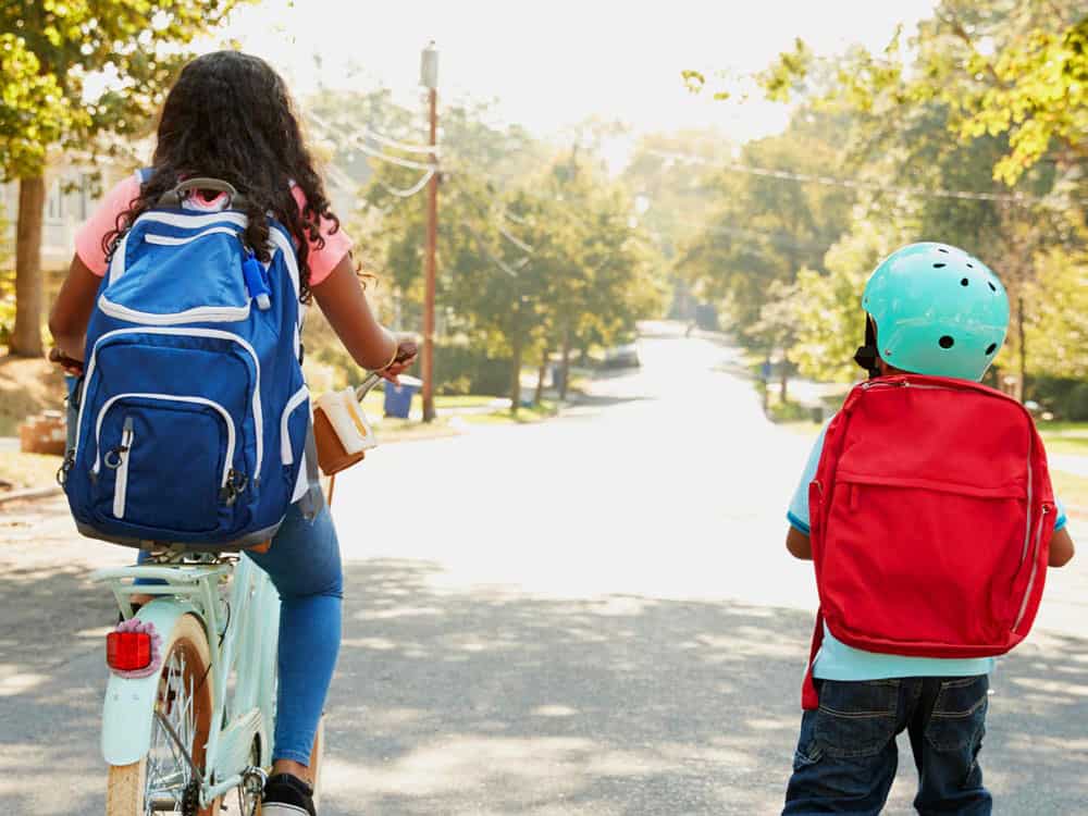 Two kids wearing school backpacks, one biking, one walking