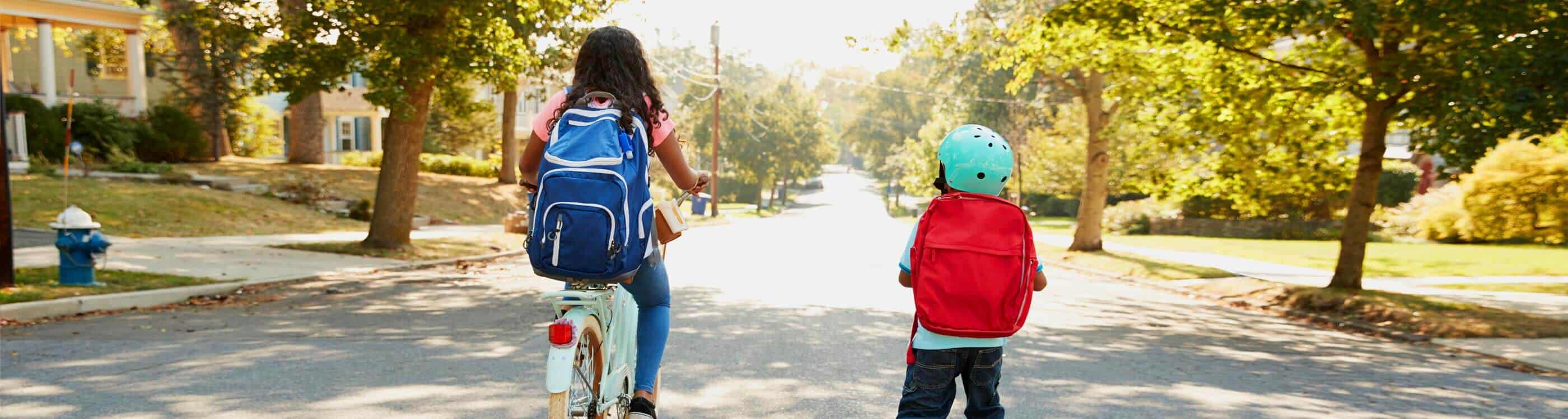 Two kids wearing school backpacks, one biking, one walking