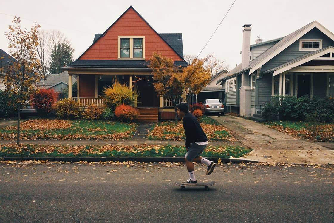 Young man skating in front of two houses