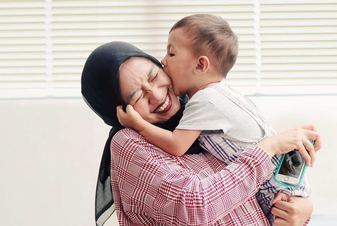 Mother holding toddler who is kissing her cheek